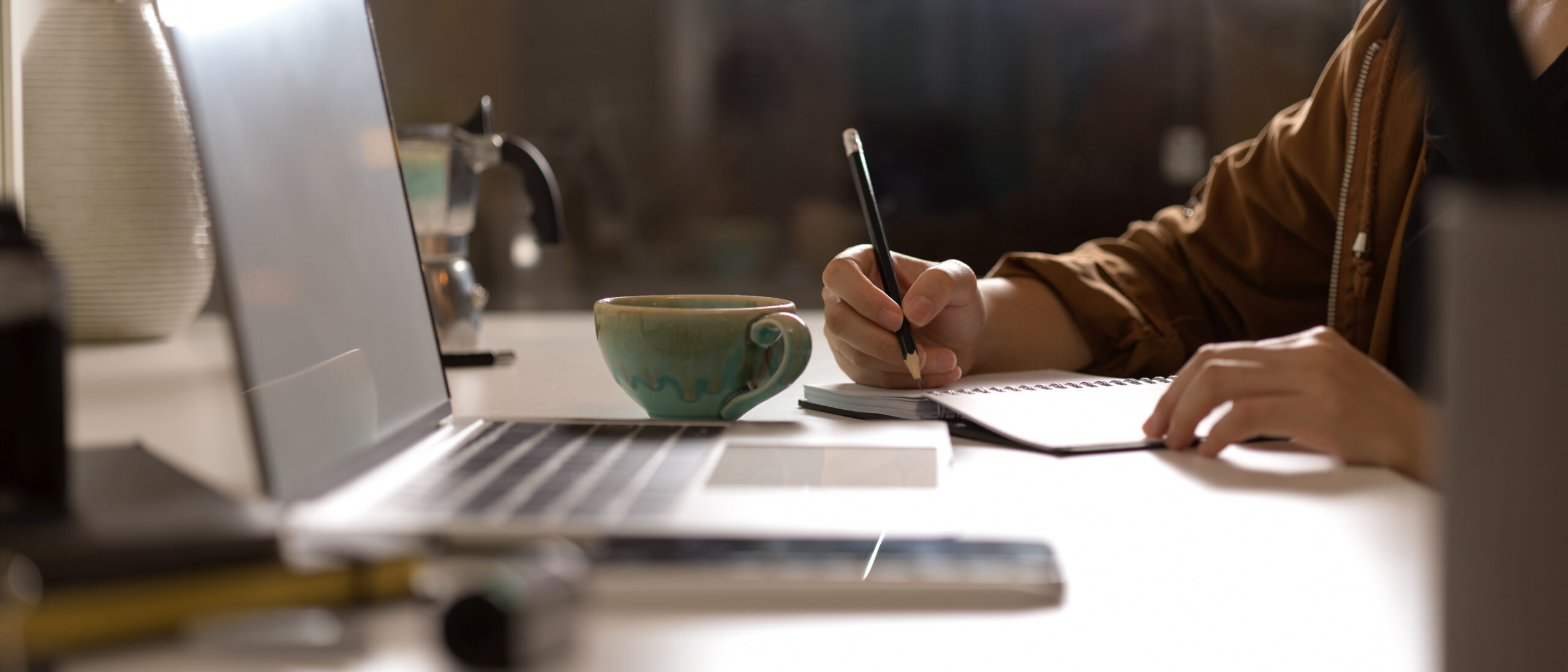 Side view of female taking note on blank schedule book on white table with mock up laptop and supplies in studio